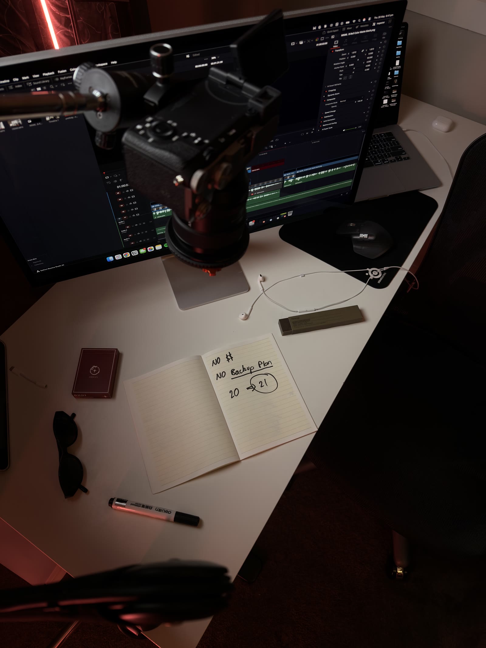 An edit desk, a camera on a monitor arm and a notebook open beside it.