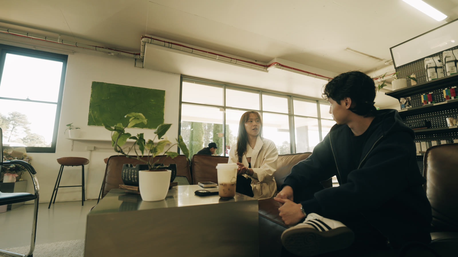 Two people in conversation on a leather sofa in a bright studio.